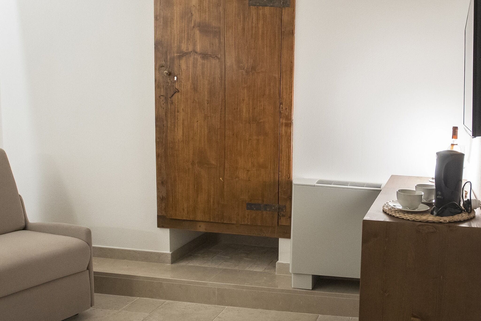 A room with a wooden wardrobe, a white sofa, a small table with a cup and saucer, and a radiator.