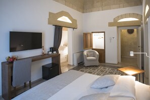 A hotel room with a bed, a desk with a flat-screen TV, a chair, and a bathroom door. - Palazzo Montemurro (Matera)