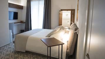 A hotel room with a bed, a bedside table, a TV mounted on the wall, and a window with curtains.