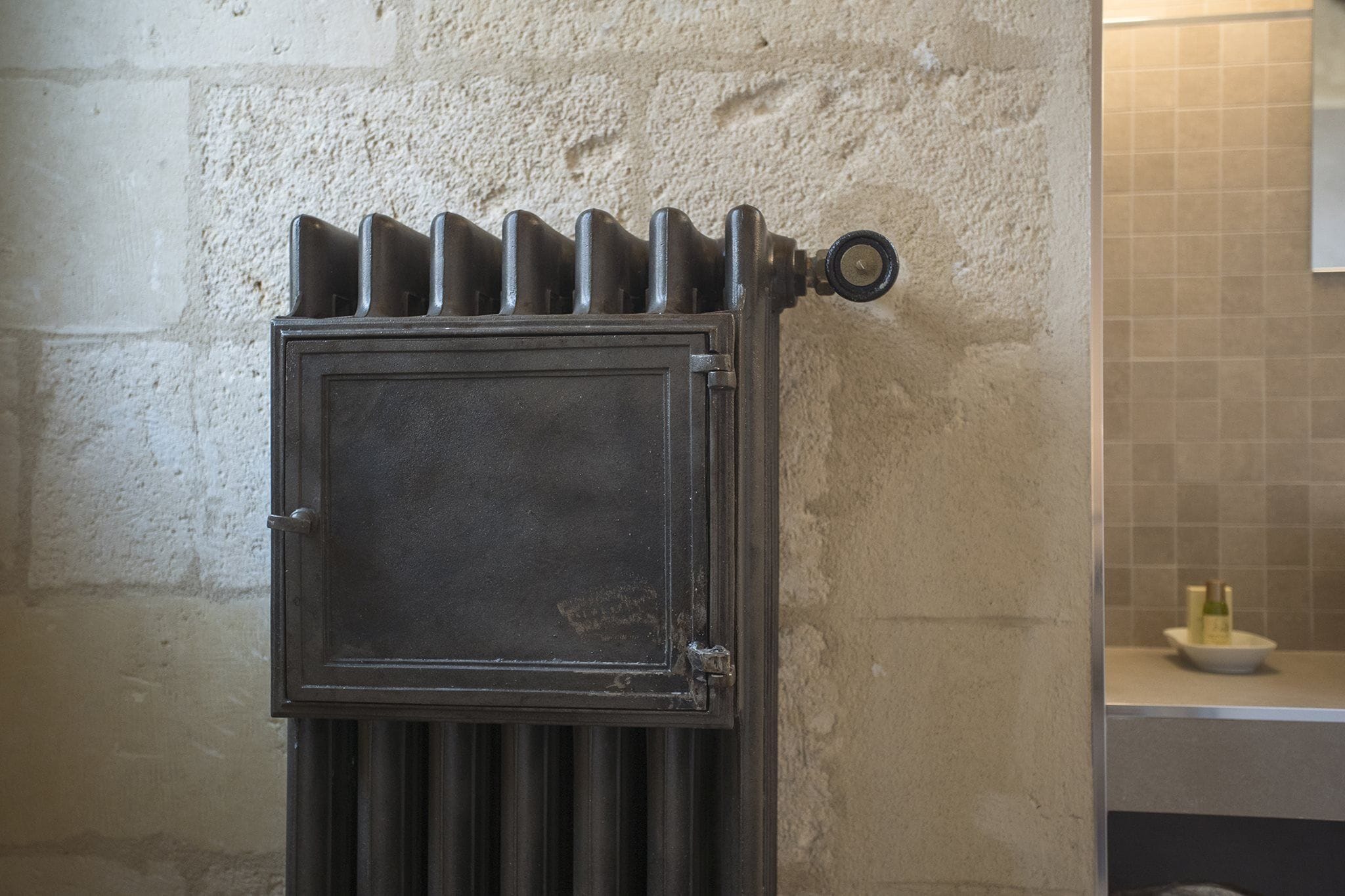 A radiator in a room with a tiled wall and a countertop with a bottle and a bowl.
