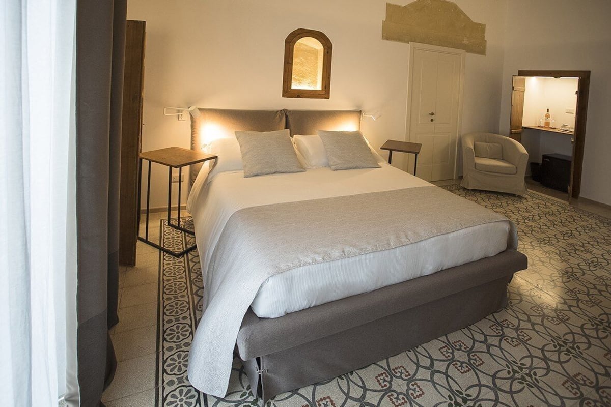 Ein Schlafzimmer mit einem großen Bett, Nachttischen, einem Sessel, einem Spiegel und einem gemusterten Boden.