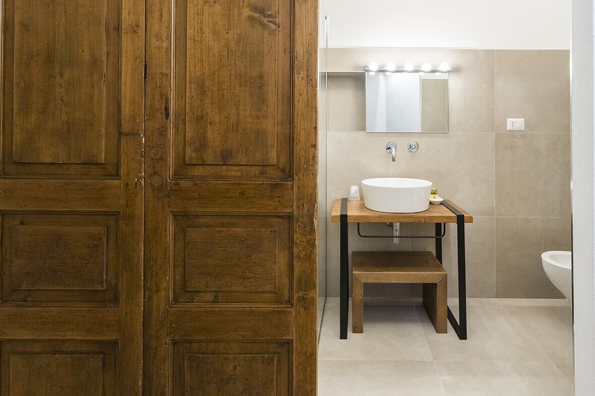 Un baño con puerta de madera, un lavabo sobre un pedestal de madera y un espejo encima del lavabo.
