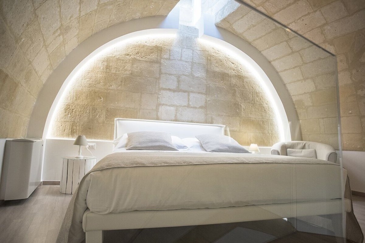 Ein modernes Schlafzimmer mit gewölbter Steindecke, einem großen Bett mit weißen Bettwäsche und einem kleinen Nachttisch mit Lampe.