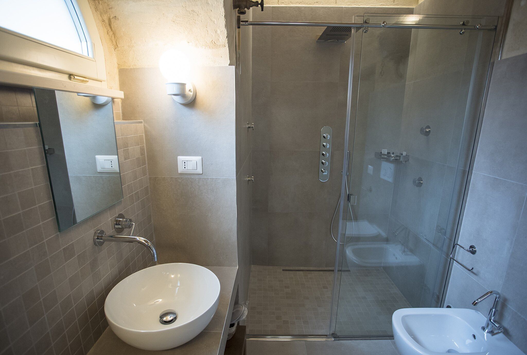 Un bagno moderno con doccia vetro, un lavabo sospeso e un lavabo su piedistallo.