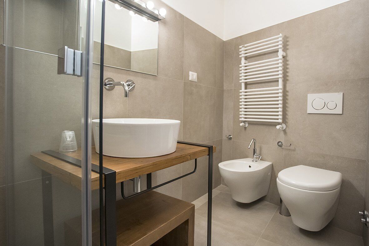 A modern bathroom with a glass shower enclosure, a wooden vanity with a white sink, a bidet, and a toilet.