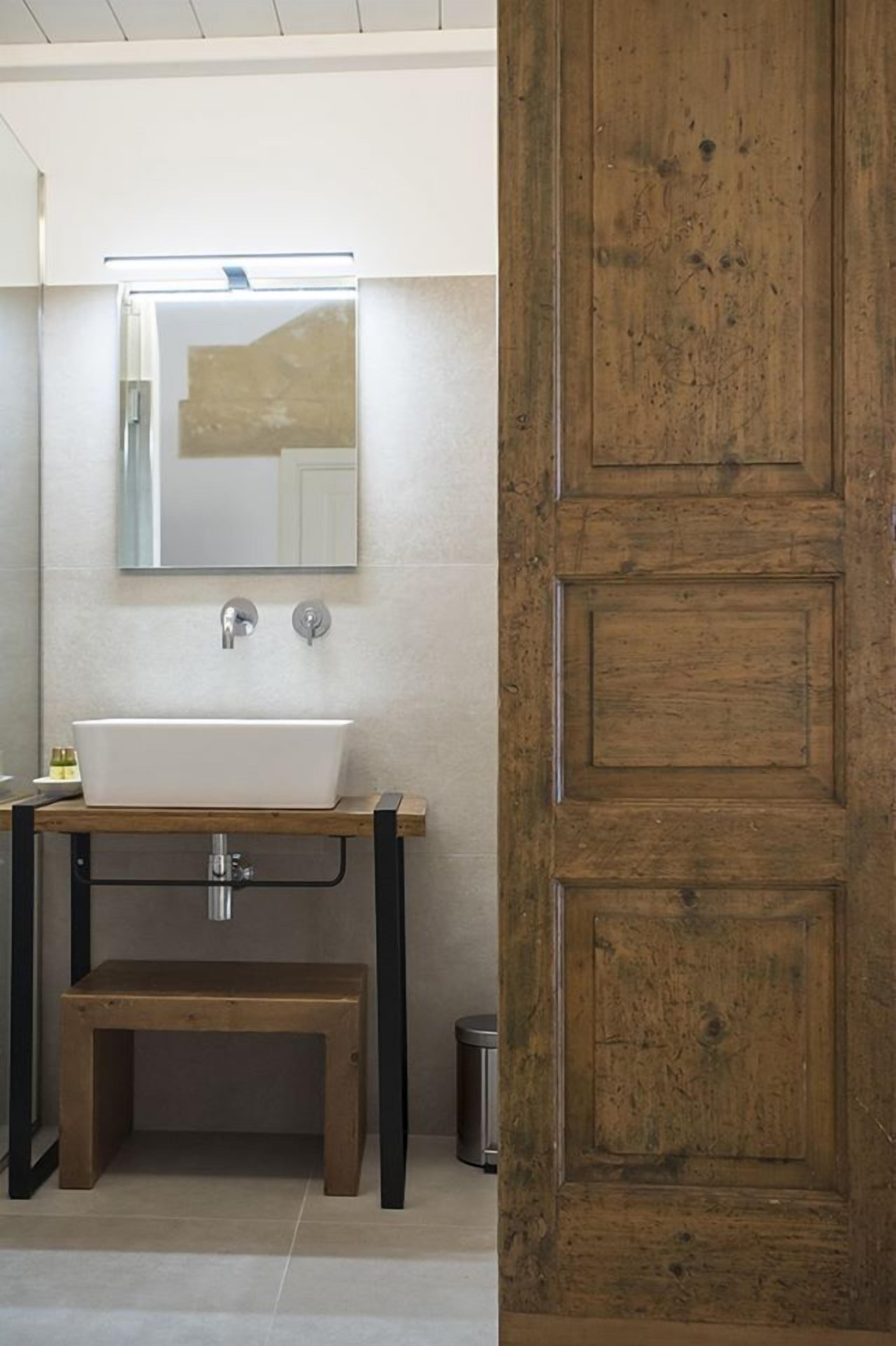 A bathroom with a wooden bench, a white sink, and a mirror above it.