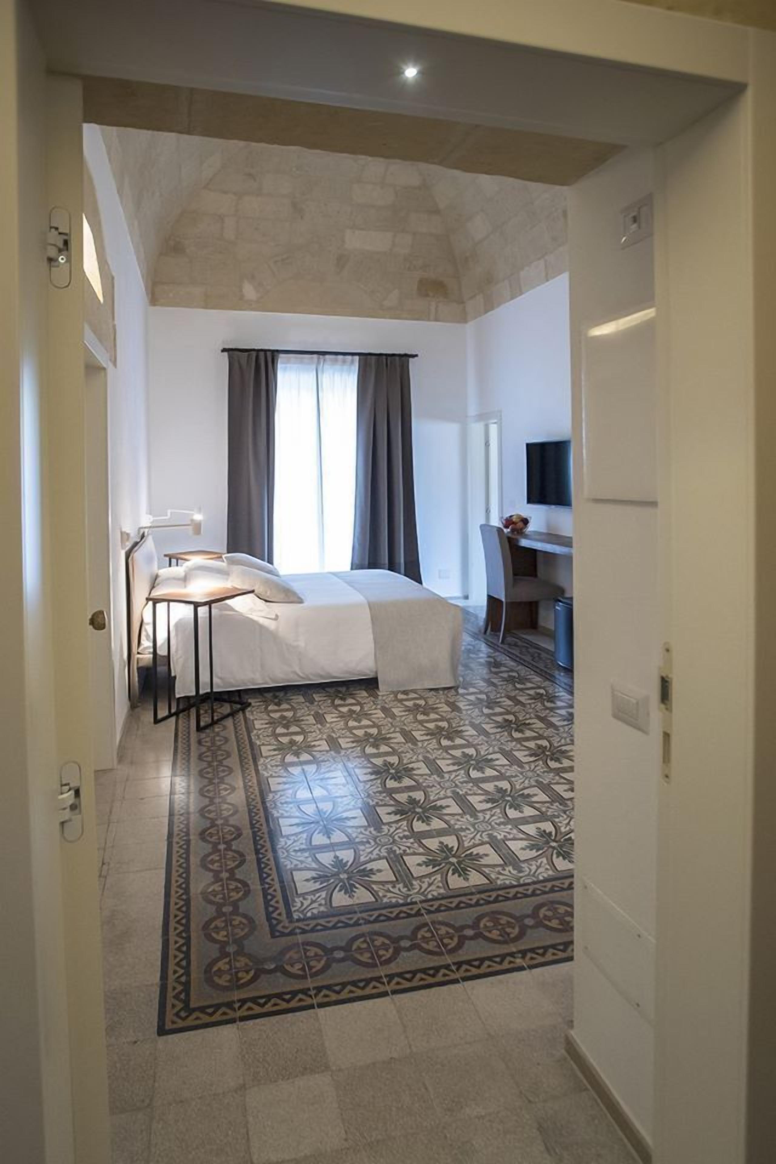 Een hotelkamer met een bed, een bureau, een stoel, een televisie en een kamerbreed tapijt met een patroon.