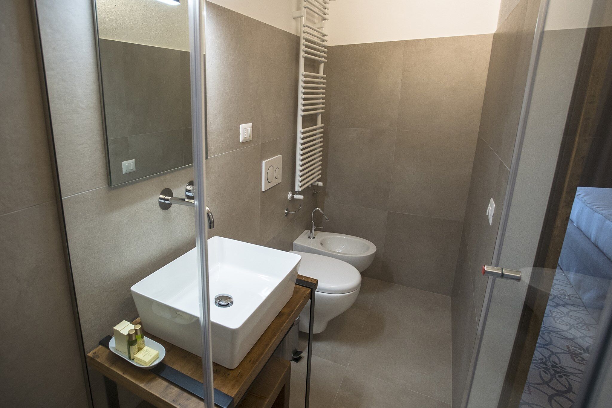 A modern bathroom with a large mirror, a rectangular sink, a bidet, and a towel rack.