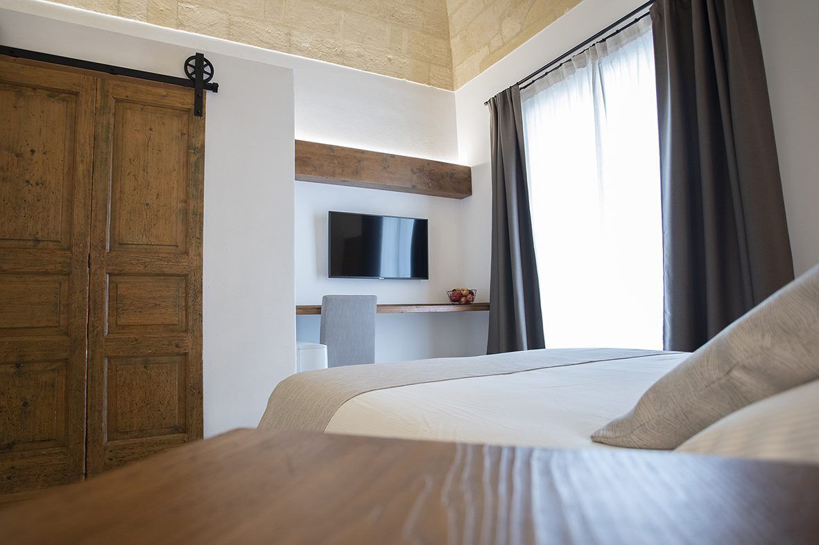 Hotelkamer met een groot bed, een houten garderobe, een flatscreen televisie aan de muur, een klein bureau met stoel, en een raam met gordijnen.