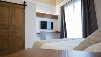 Hotelkamer met een groot bed, een houten garderobe, een flatscreen televisie aan de muur, een klein bureau met stoel, en een raam met gordijnen.
