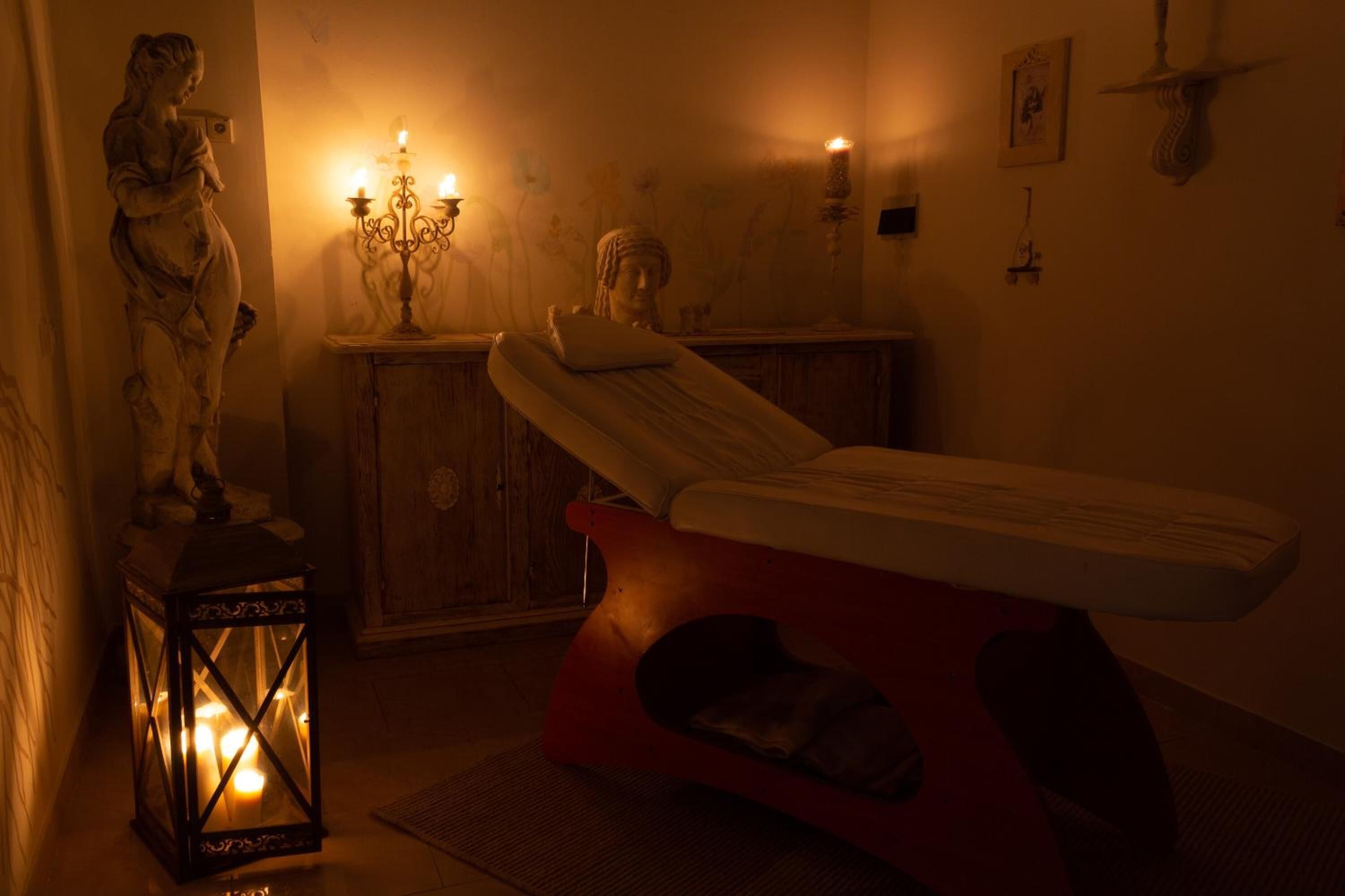 A dimly lit room with a massage table, a statue, and a candle-lit wall.