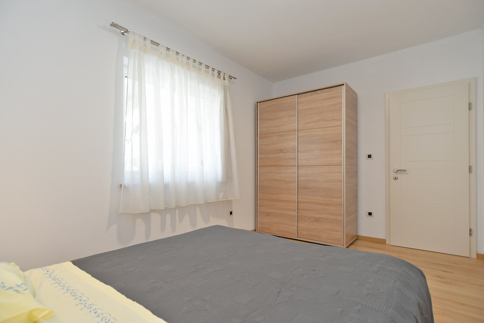 A bedroom with a bed, a wardrobe, a door, and a window with curtains.
