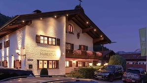 Un hotel con fachada de piedra, balcones de madera y montañas al fondo.
