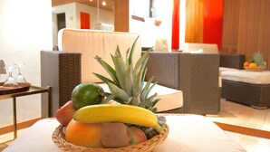 Una cesta de frutas sobre una mesa en el vestíbulo de un hotel, con muebles de mimbre y vista al interior.
