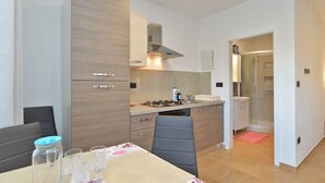A compact kitchen with a gas stove, a built-in oven, and a microwave. There is a dining area with a table and chairs, and a small bathroom with a shower and sink. - Apartment 1701/17690 (Istria - Fažana), 300m from the beach (Fažana)