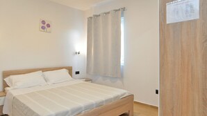 A bedroom with a wooden bed, white bedding, a window with curtains, and a wooden door. - Apartment 1701/17690 (Istria - Fažana), 300m from the beach (Fažana)
