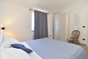 A bedroom with a bed, a chair, a window with curtains, and a wall-mounted light.