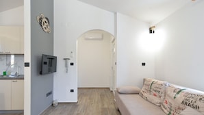 A modern living room with a sofa, a kitchen area with a sink and cabinets, and a hallway leading to a door.