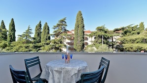 A table with a white tablecloth and two chairs, set on a terrace with a view of trees and buildings.