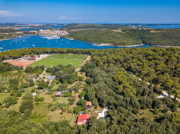 Vue aérienne d’une zone côtière comprenant un port de plaisance, un terrain de sport et une forêt dense.