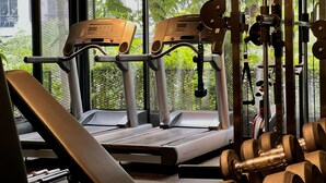 A gym with exercise equipment, including treadmills and dumbbells, and large windows with a view of greenery.