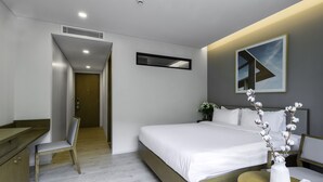 A modern hotel room with a bed, a desk, and a chair. There is a door leading to another room and a window with a view.