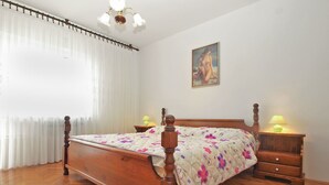 A bedroom with a wooden bed, floral bedding, two bedside tables with lamps, a painting on the wall, and a window with sheer curtains.