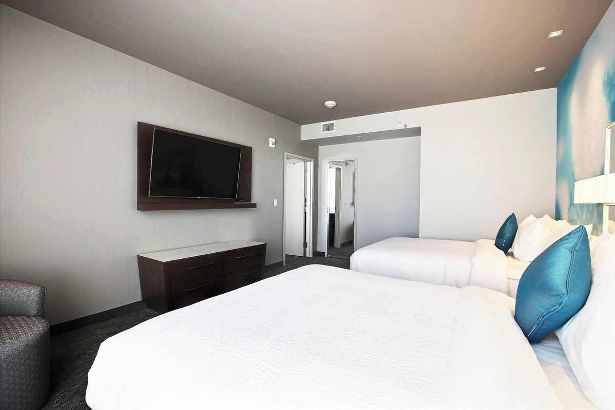 Ein Hotelzimmer mit einem großen Bett, einem an der Wand montierten Fernseher, einem Schreibtisch und einem Sessel.
