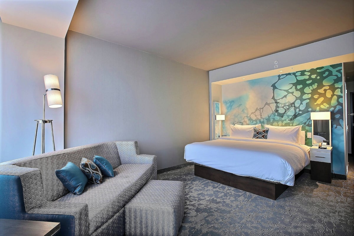 Ein modernes Hotelzimmer mit Bett, einer Couch und einer Stehlampe.