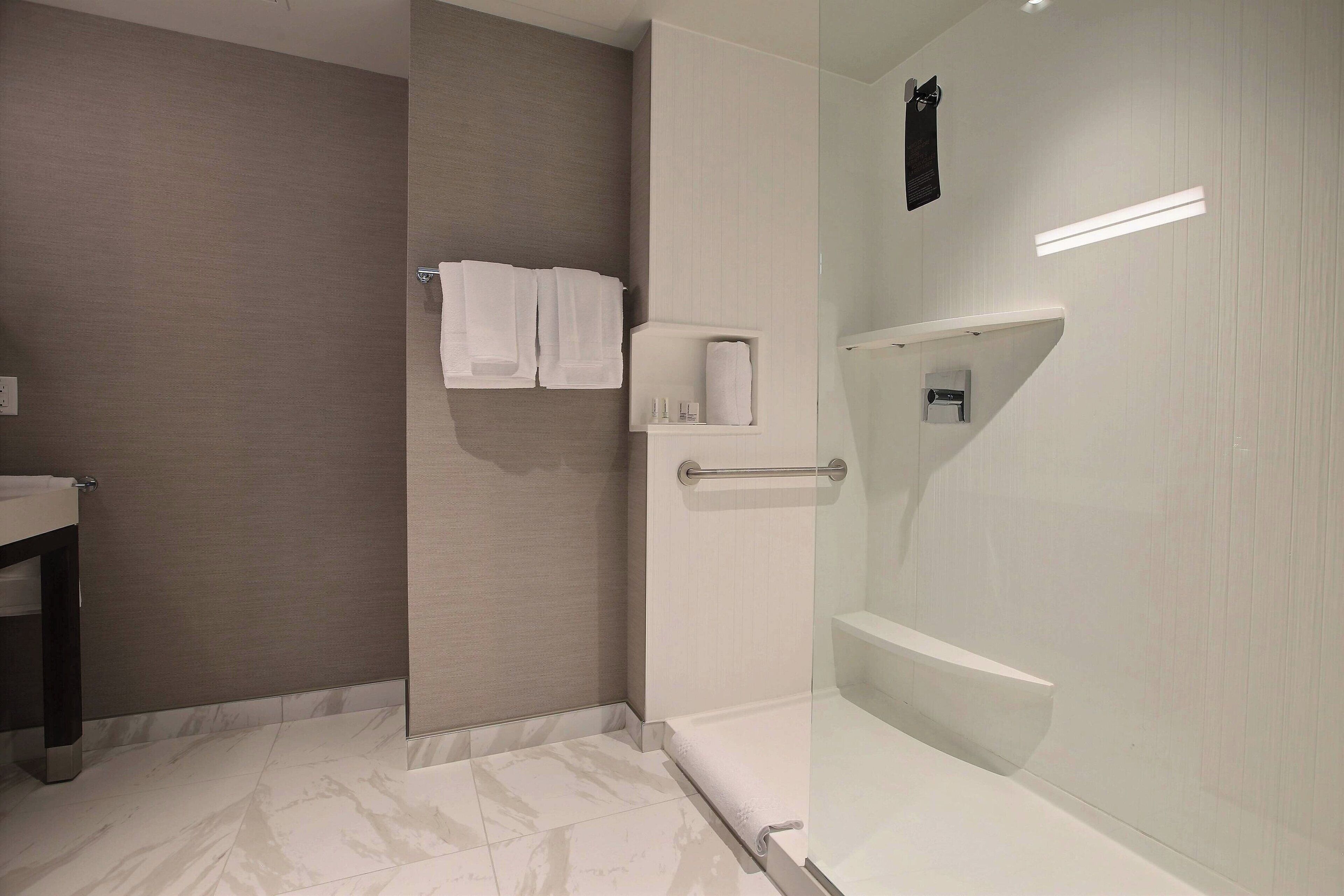 Un baño moderno con cabina de ducha de vidrio, un perchero con toallas y un pequeño estante con artículos de aseo.