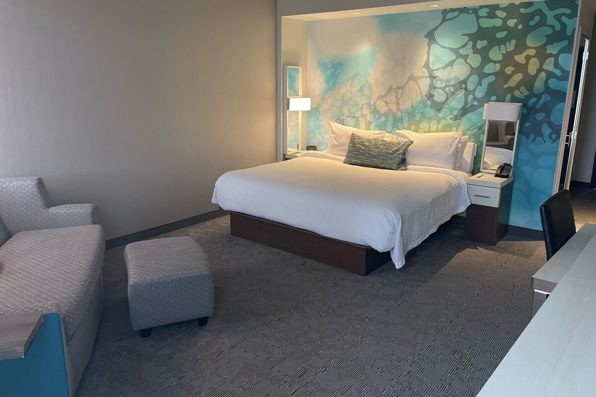 Ein Hotelzimmer mit einem Bett, einem Schreibtisch, einem Sessel und Teppichboden.