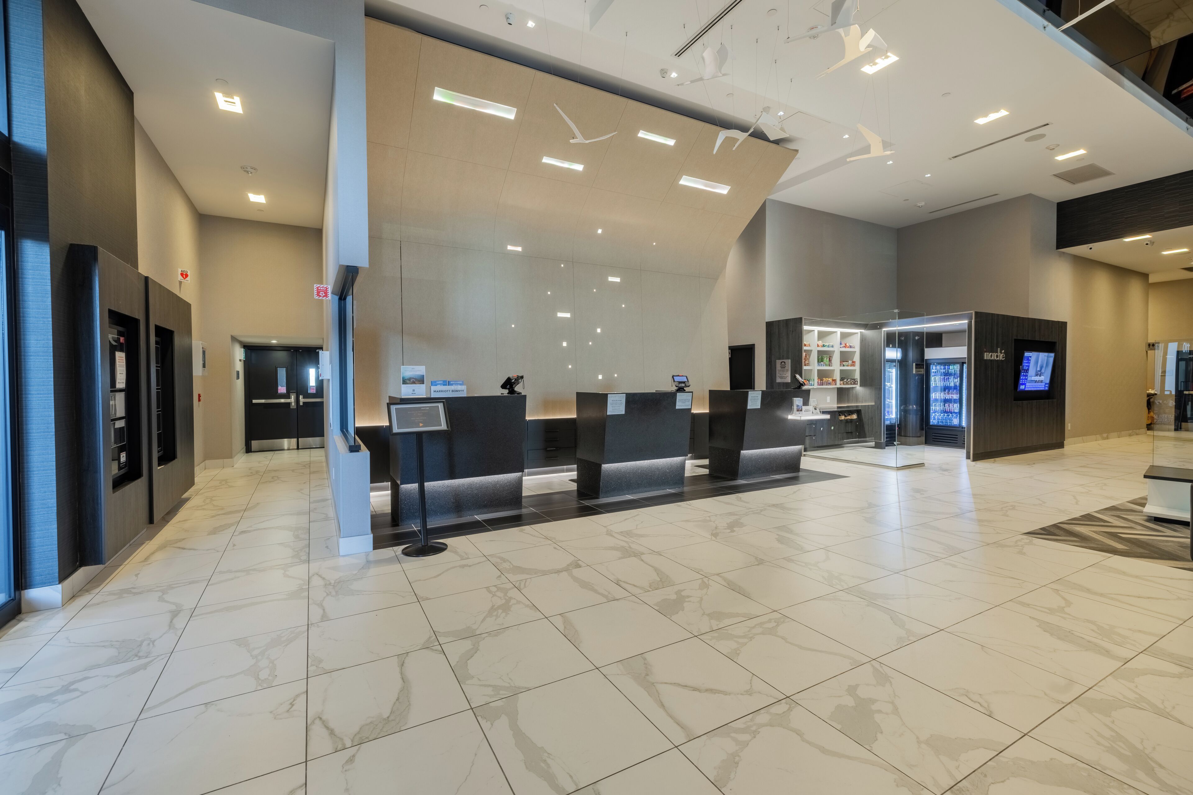 Un moderno vestíbulo de hotel con piso de mármol, mostradores de recepción y una gran pantalla digital.