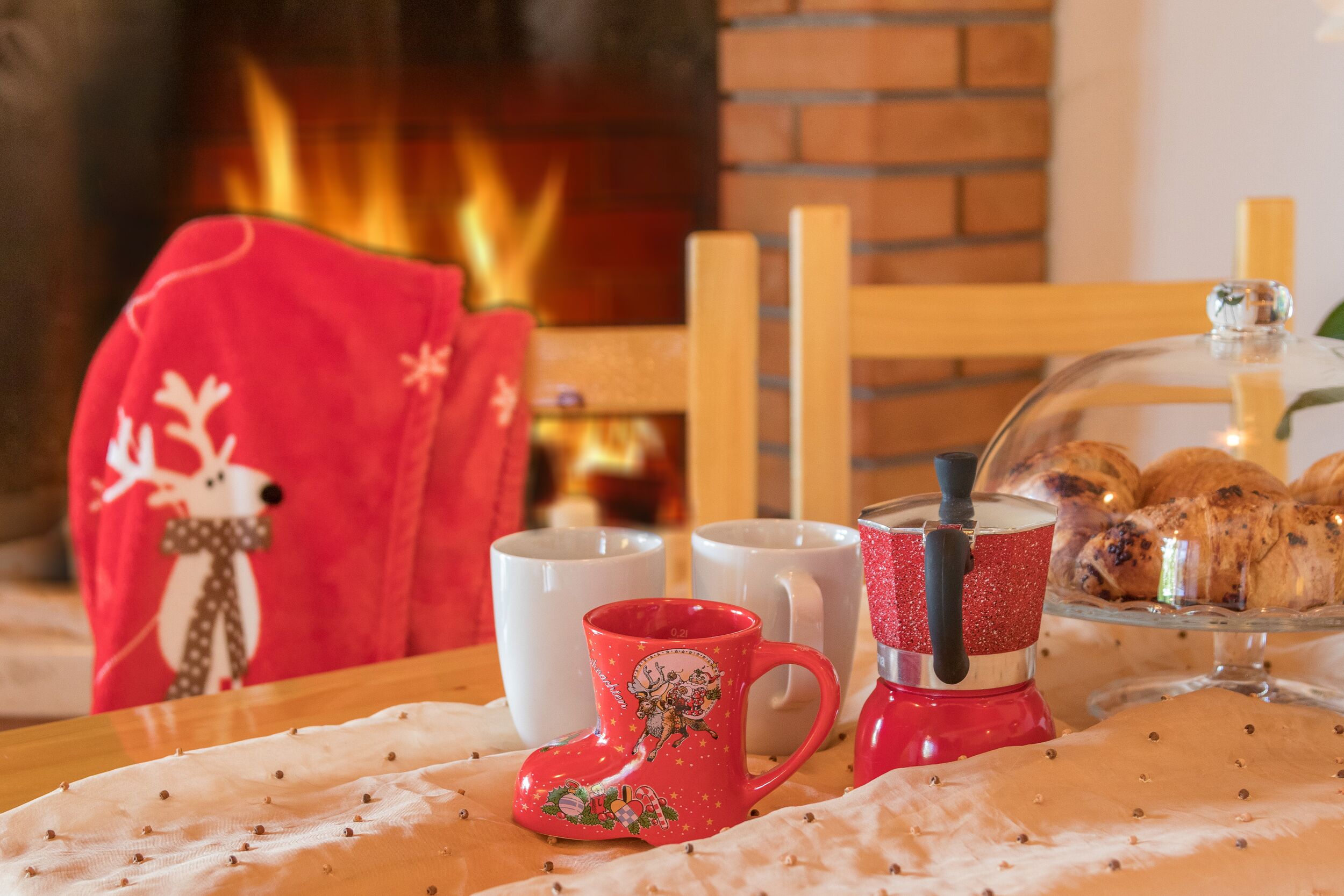 A cozy indoor setting with a fireplace, a table with a red mug, white mugs, and a glass display case with pastries.