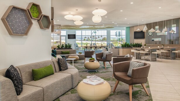 A modern lounge area with sofas, chairs, a round ottoman, and a dining area with tables and chairs. - Element by Marriott San Jose Milpitas (Milpitas)