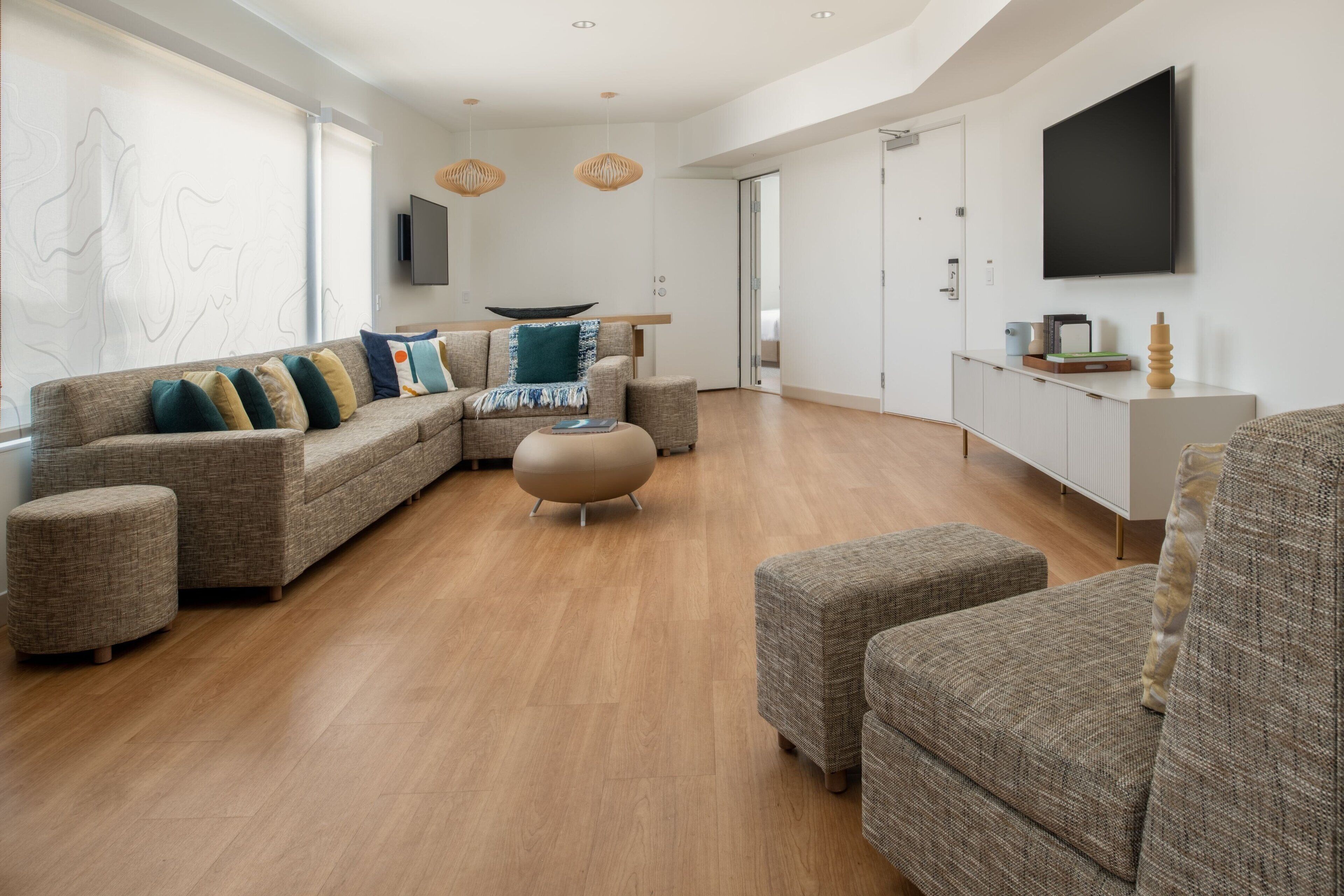 Un salon moderne avec un canapé d’angle, des poufs et un téléviseur à écran plat fixé au mur.