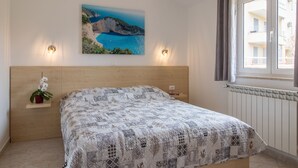 A bedroom with a bed, a nightstand, a wall-mounted painting, and a window with curtains. - Apartment 1706/17819 (Istria - Liznjan), 1250m from the beach (Liznjan)