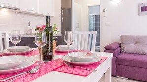 A dining area with a table set for two, white cabinets, a purple sofa, and a bottle of wine. - Apartment 1706/17820 (Istria - Liznjan), 1250m from the beach (Liznjan)