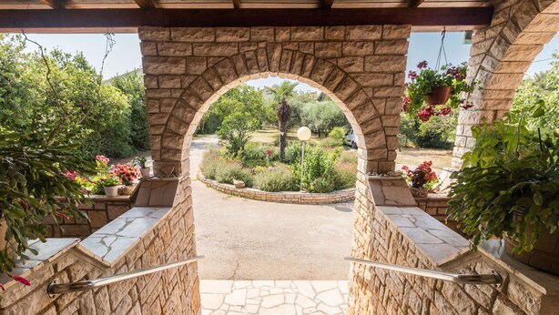 A stone archway leading to a garden with a paved path, surrounded by greenery and potted plants. - Apartment 1706/17820 (Istria - Liznjan), 1250m from the beach (Liznjan)