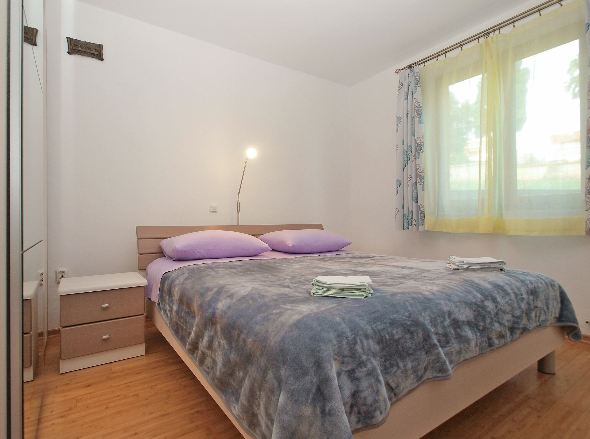 A bedroom with a bed, a bedside table, a lamp, and a window with curtains.
