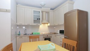Ett kompakt kök med vita skåp, en mikrovågsugn, ett kylskåp och ett matbord med stolar.