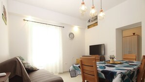 A modern living room with a sofa, dining table, chairs, a TV, and a clock on the wall. - Apartment 1707/17625 (Istria - Banjole), 100m from the beach (Banjole)