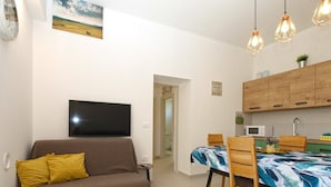 A living room with a sofa, a dining table with chairs, a TV mounted on the wall, and wooden cabinets in the kitchen area. - Apartment 1707/17625 (Istria - Banjole), 100m from the beach (Banjole)