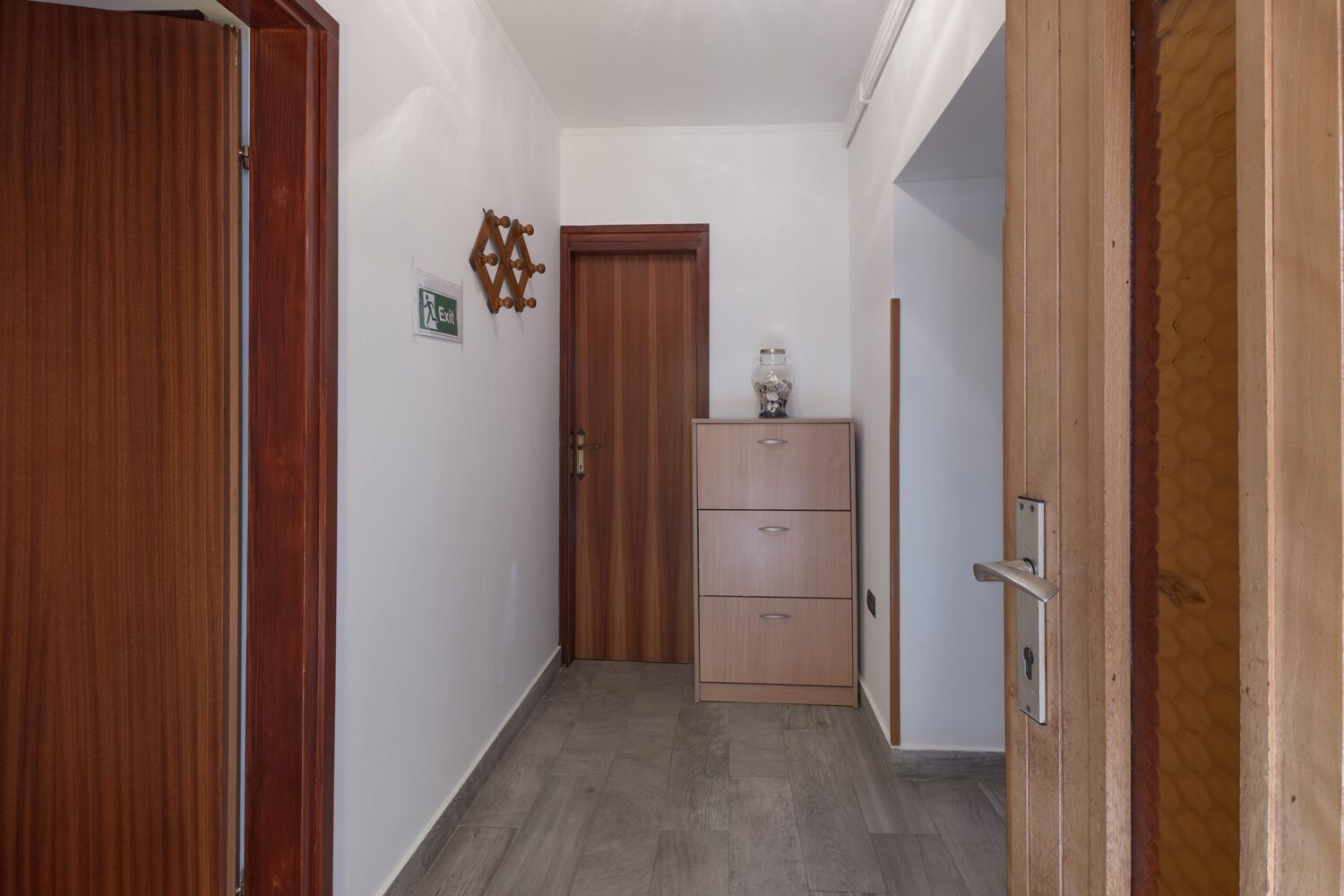 A hallway with wooden doors, a cabinet with drawers, and a wall-mounted light fixture.