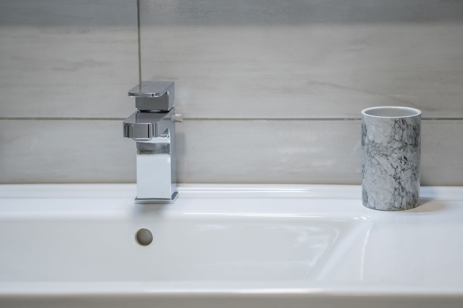 Un lavabo de salle de bain avec un robinet chromé et une tasse en marbre posée sur le comptoir.