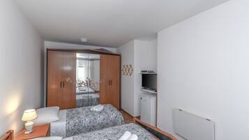 Habitación de hotel con dos camas, un armario, un televisor y un refrigerador pequeño.