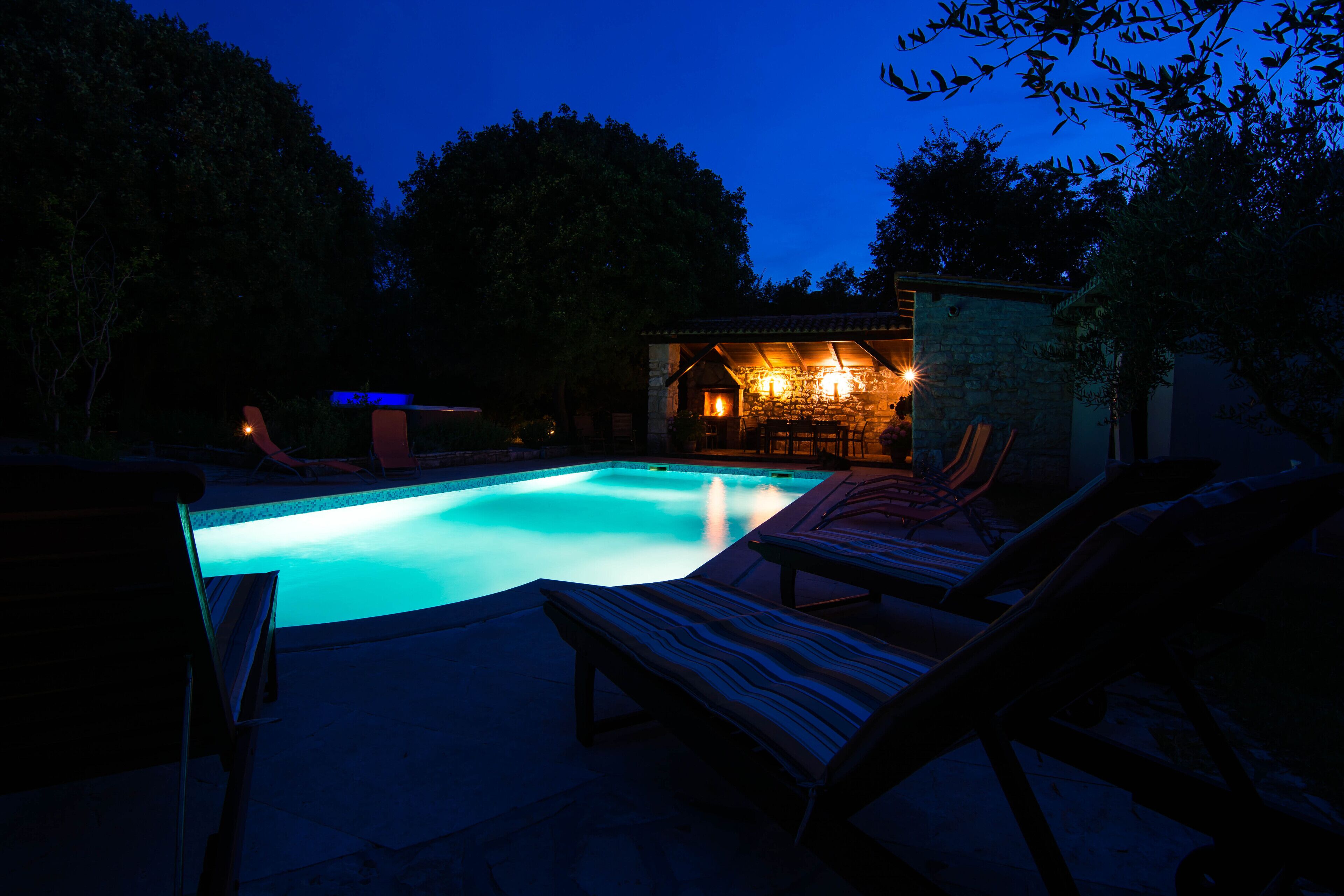 Una piscina con sillas de descanso y una zona de estar cubierta al anochecer.