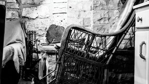 A rustic kitchen with a wicker chair, a tiled floor, and a stone wall.