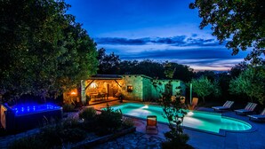 A stone building with a pool and lounge chairs, surrounded by trees and a stone pathway.