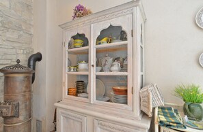 Antique kitchenware on display in a charming cabinet, accompanied by a wicker chair and a potted plant.