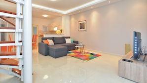 Una sala moderna con un sofá gris, un tapete colorido, una mesita redonda y un televisor sobre un mueble de madera.